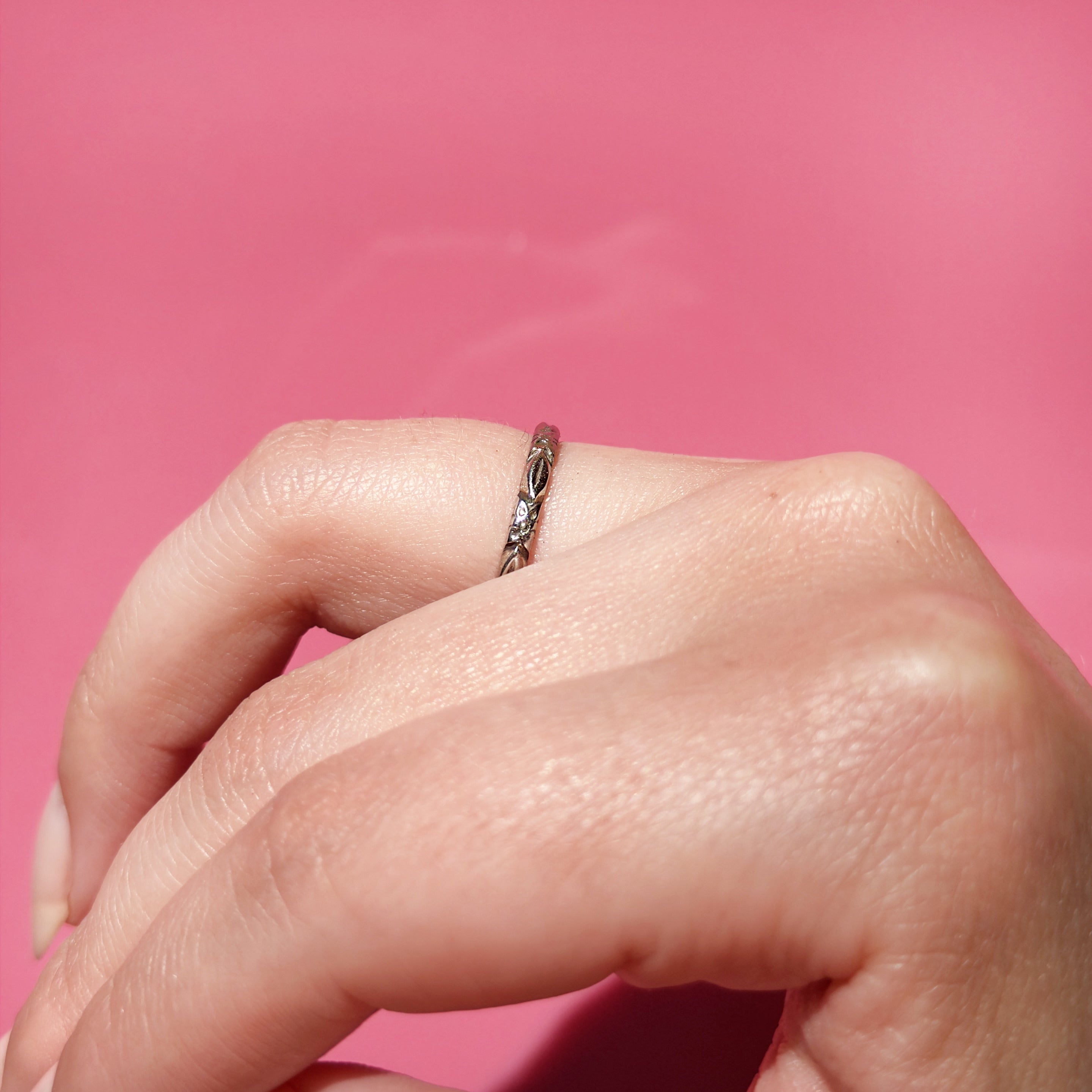 Hand wearing a white gold ring with a flower pattern on a pink background