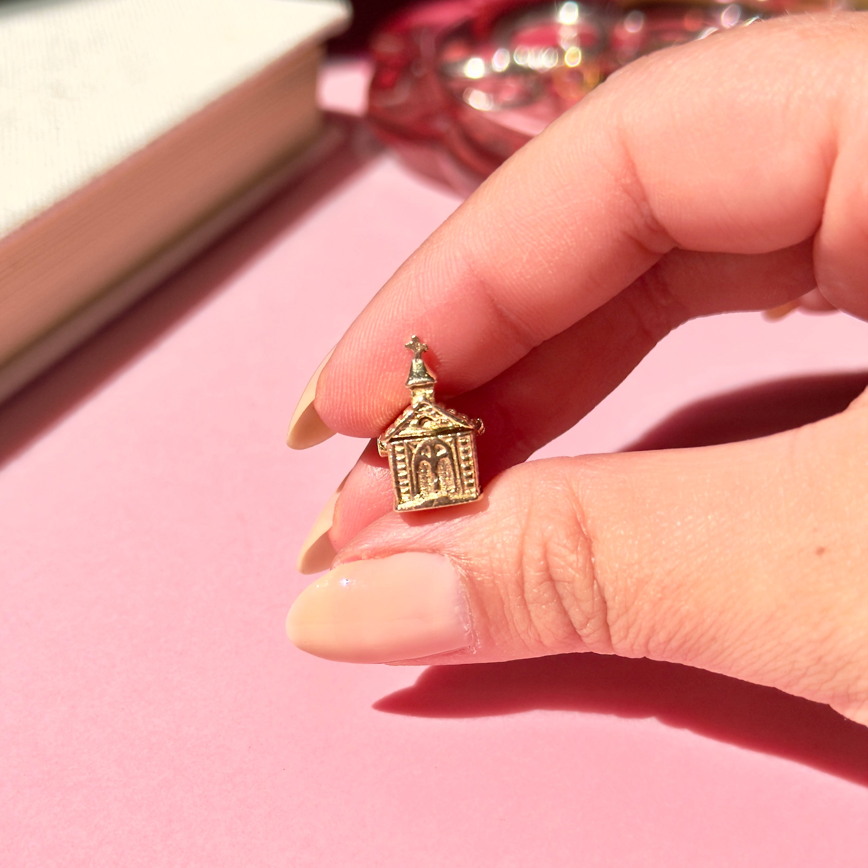 Vintage gold church charm held between fingers on a pink surface
