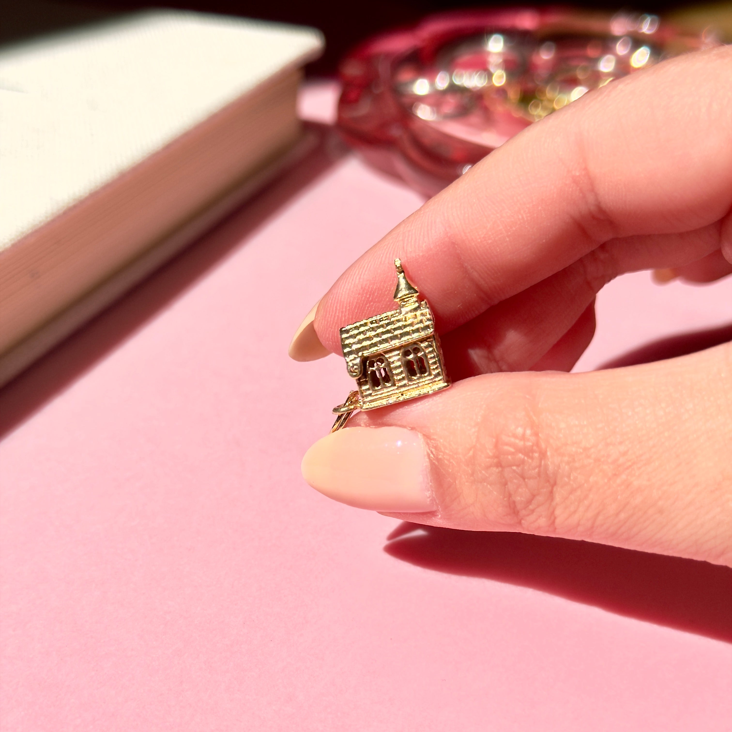 Vintage gold church charm held between fingers on a pink surface