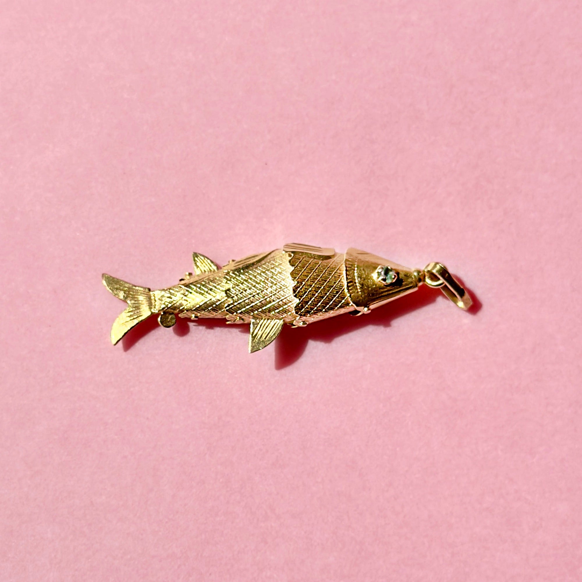 Gold fish-shaped brooch on a pink background
