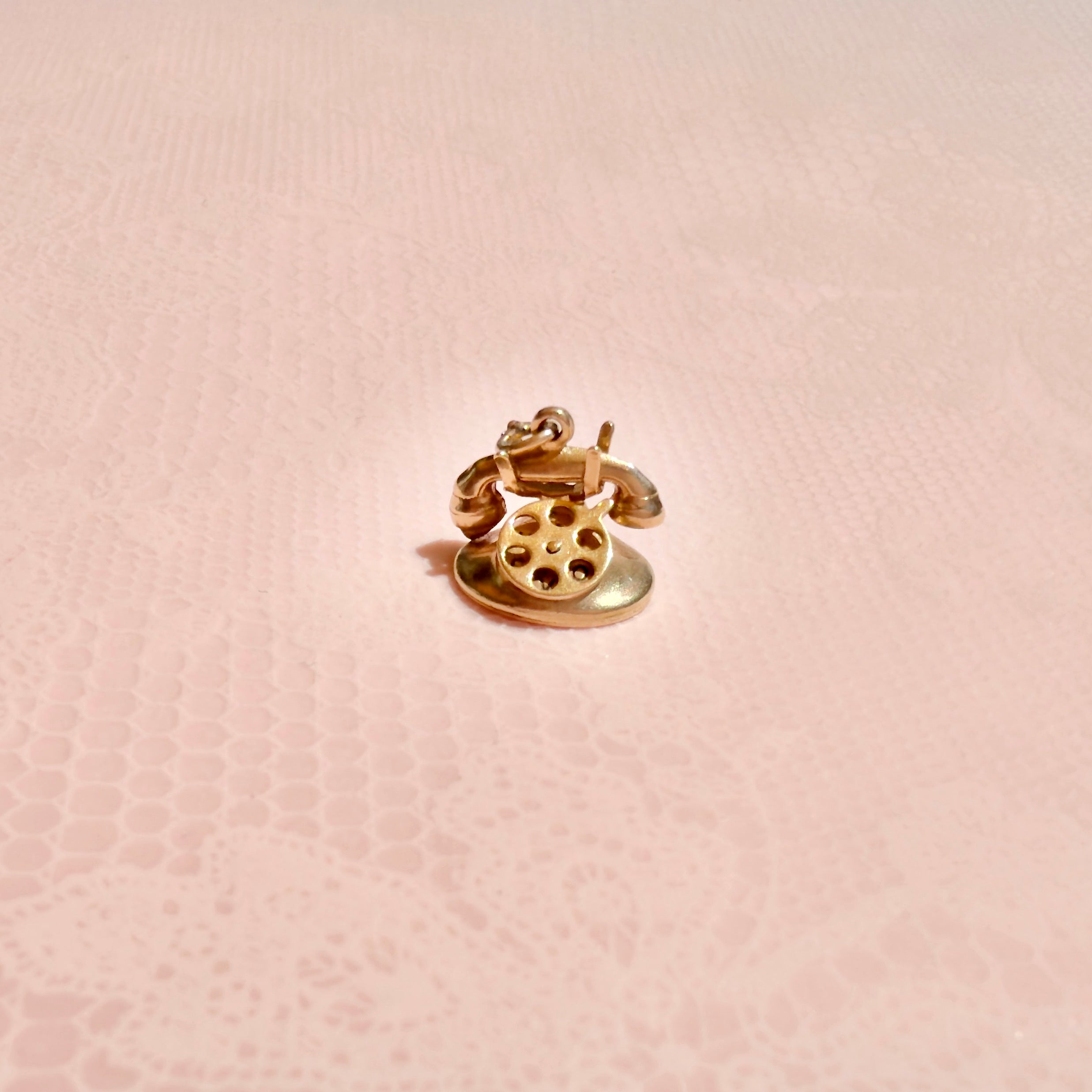 Gold phone charm on a pink textured background