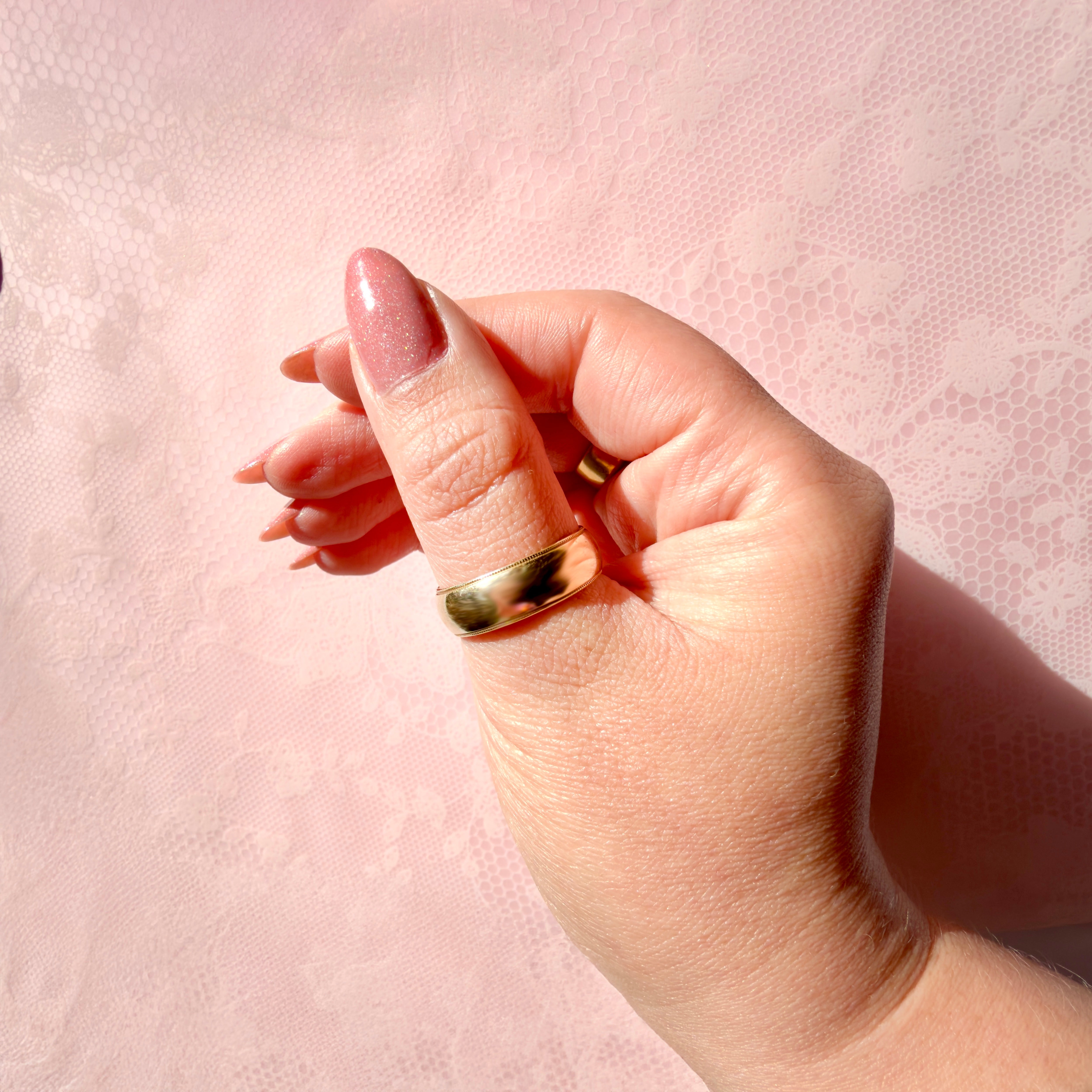 Hand wearing a gold ring on a pink textured background