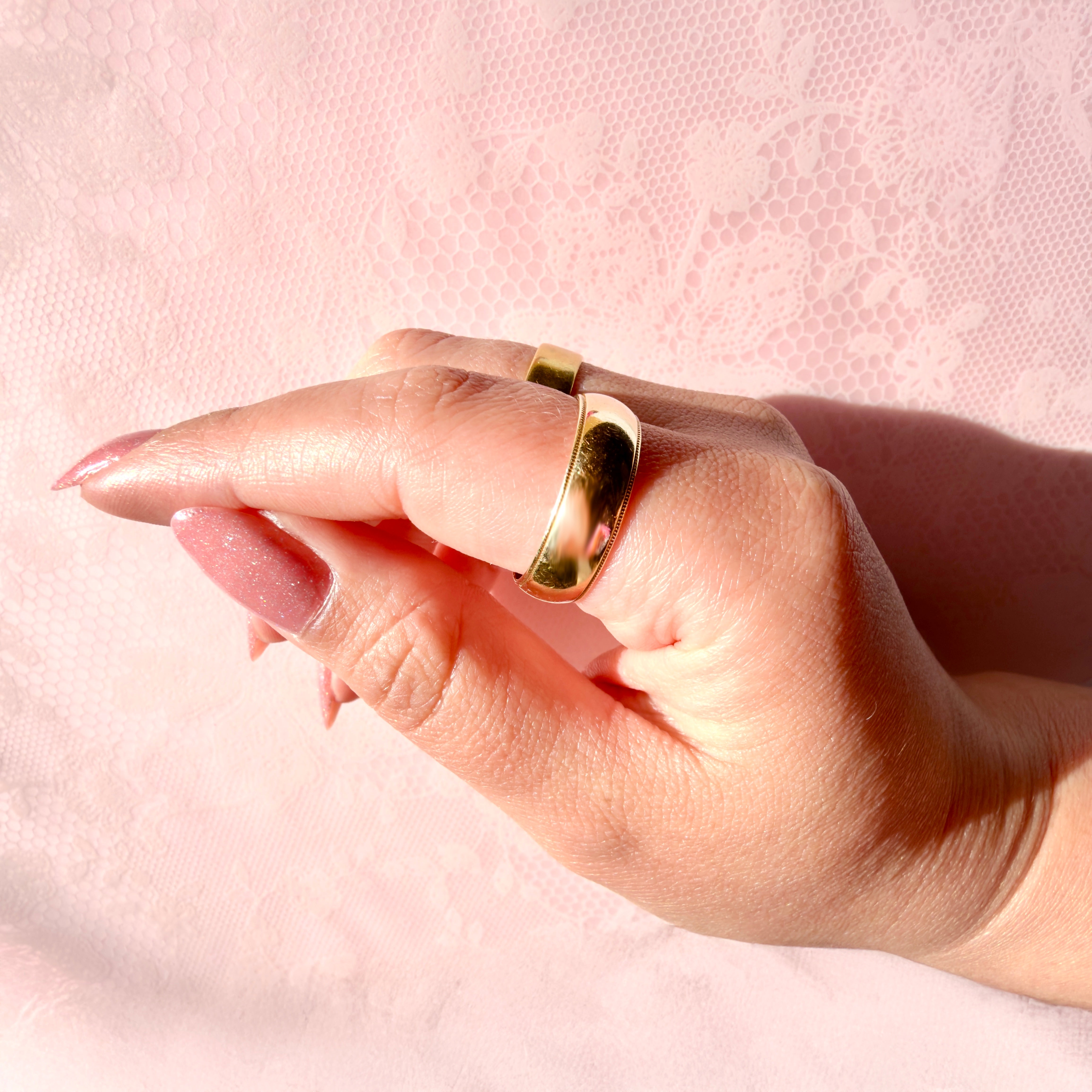 Hand wearing a gold ring on a pink textured background