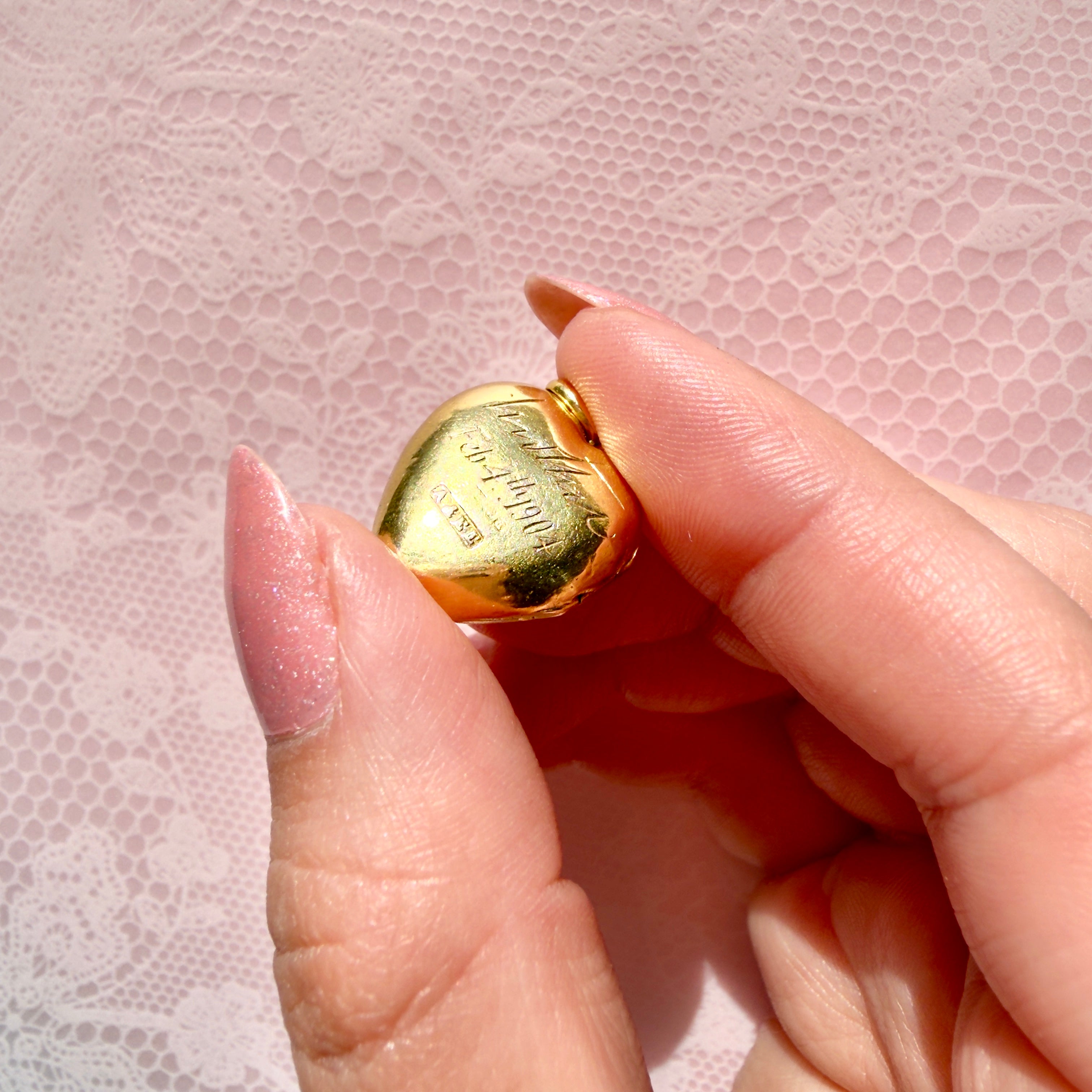 Hand holding a gold heart-shaped pendant with pearls on a pink background