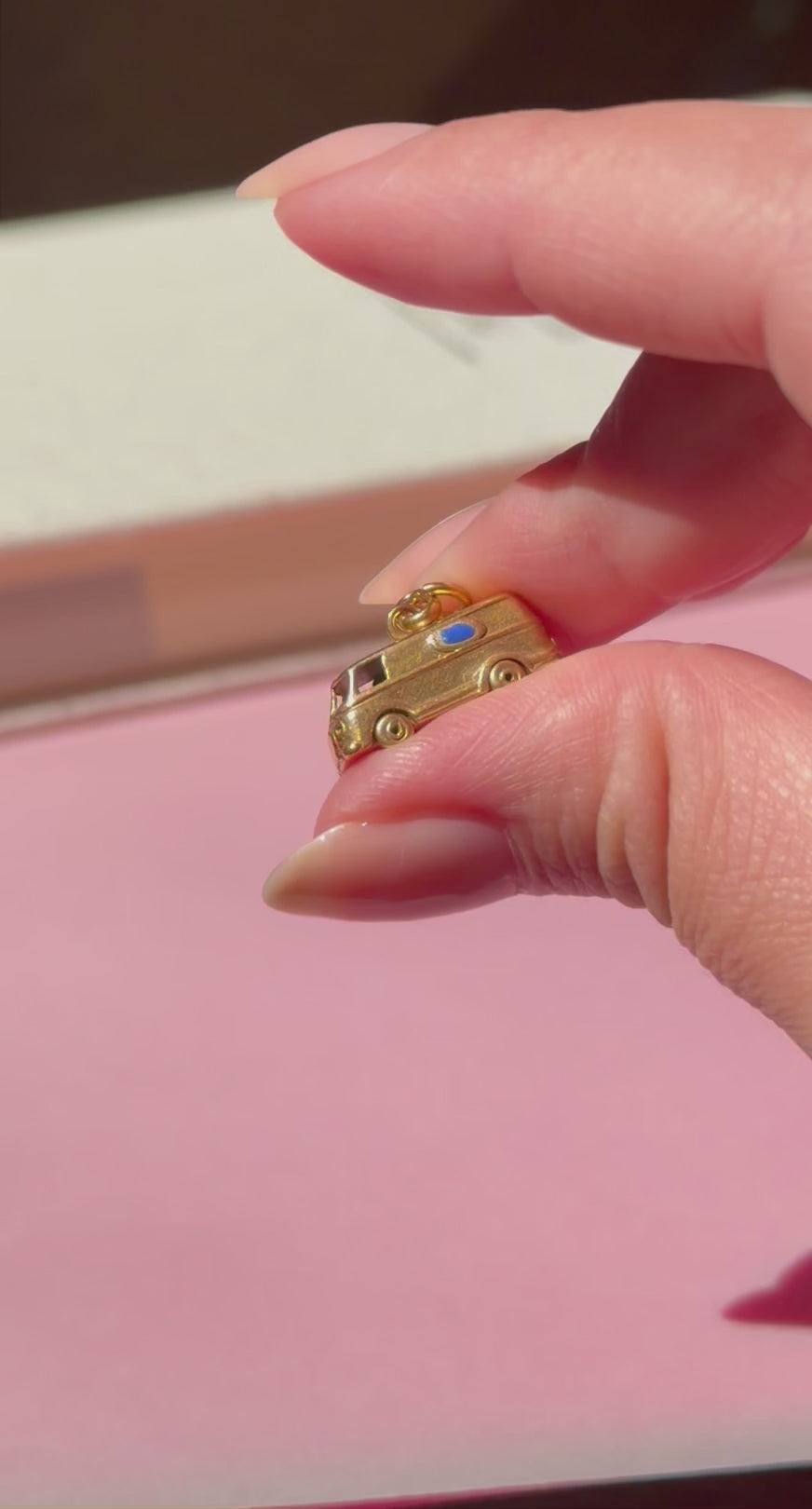Miniature gold microbus charm held by two fingers against a blurred background