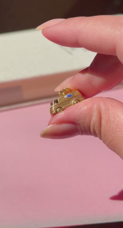 Miniature gold microbus charm held by two fingers against a blurred background