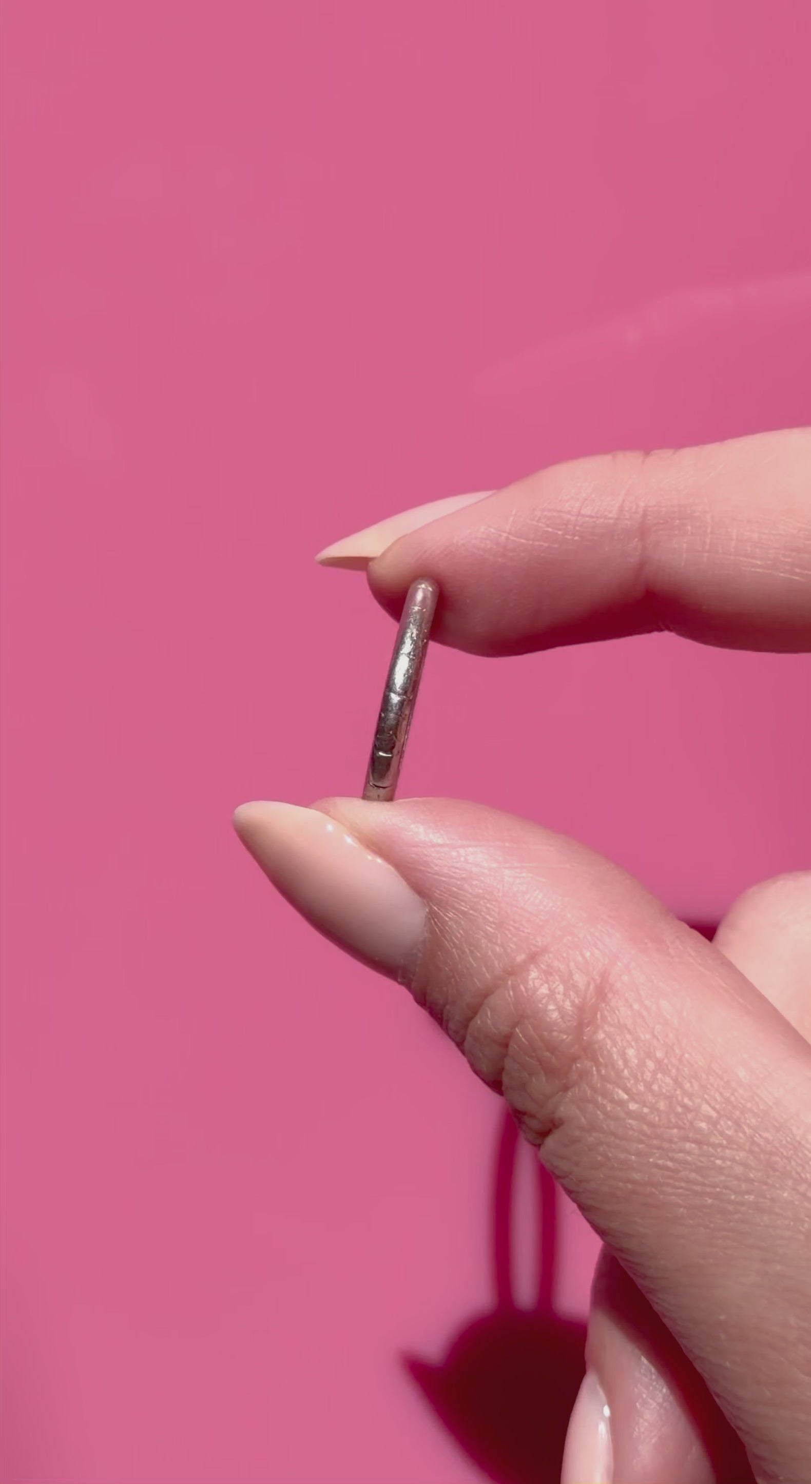 Hand holding an antique platinum ring against a pink background