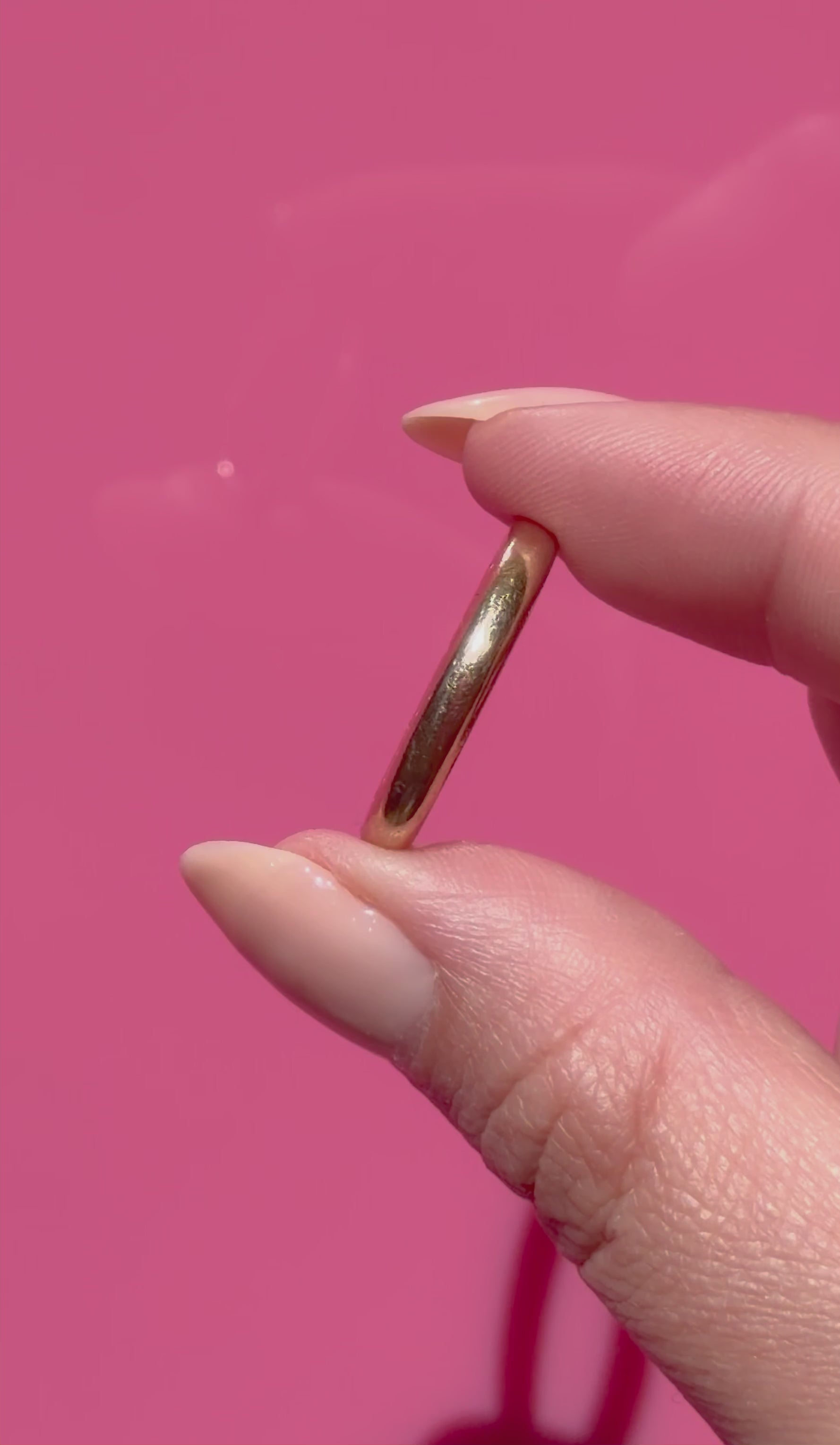 Antique gold ring held between fingers against a pink background