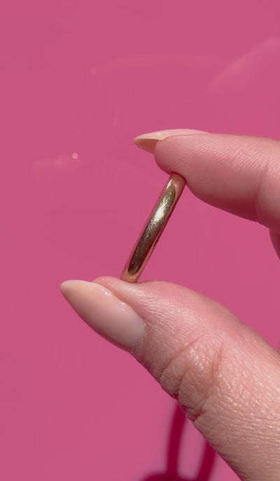 Antique gold ring held between fingers against a pink background