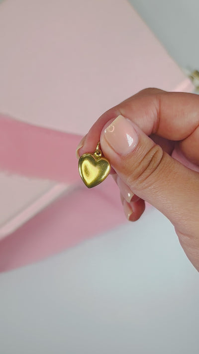 A gold heart charm held in between two fingers.