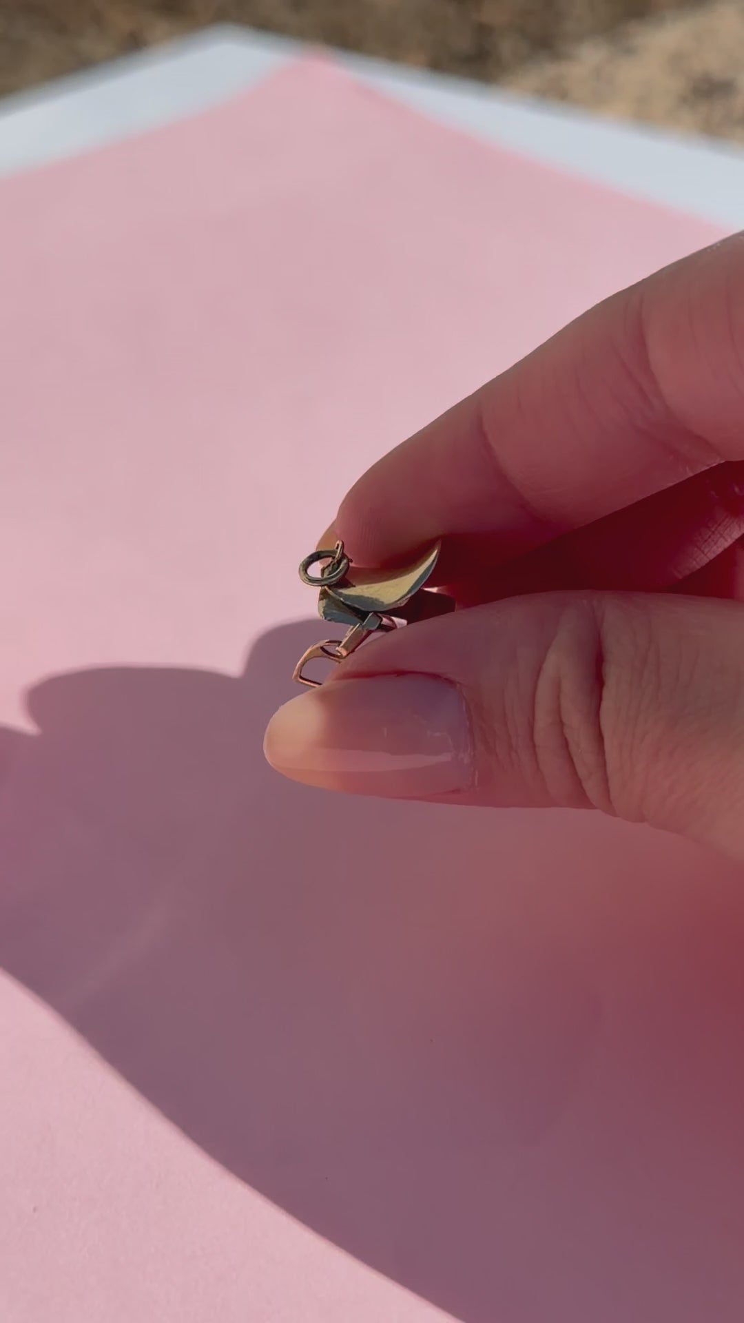A hand hold a gold saddle charm against a blurred background.