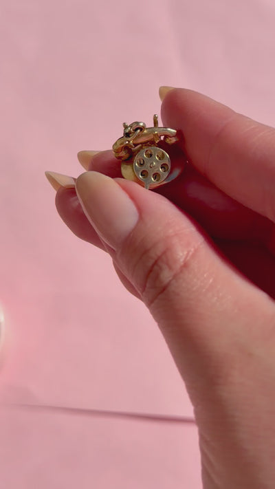 A hand holding a vintage gold charm against a pink background