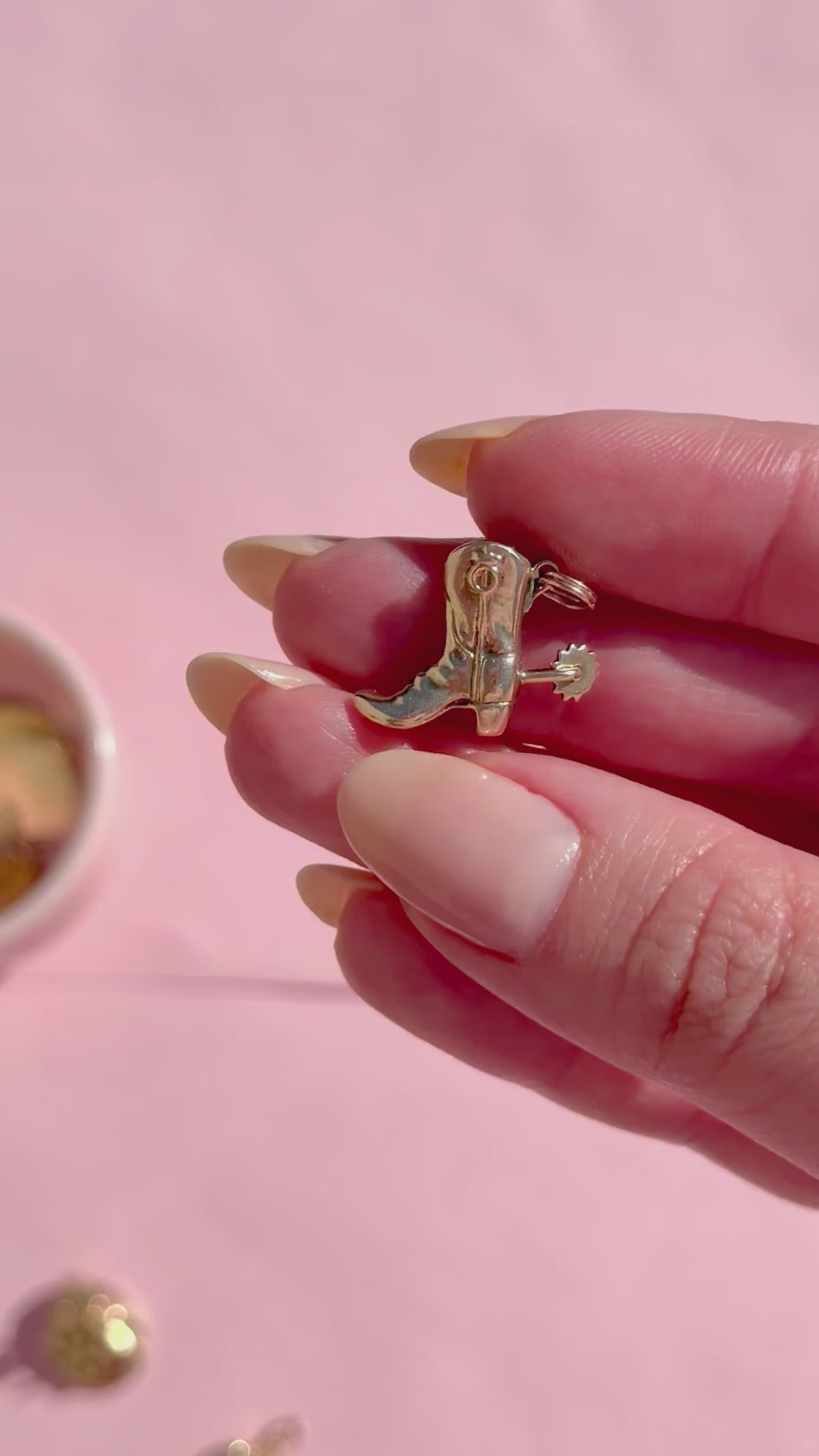 A hand holding a gold cowboy boot charm on a white background.