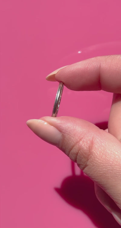 Close-up of a hand holding a vintage platinum ring against a pink background