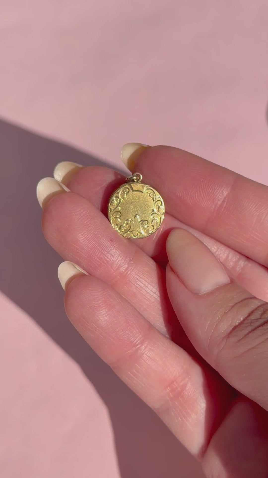 A hand holding a gold locket against a pink background