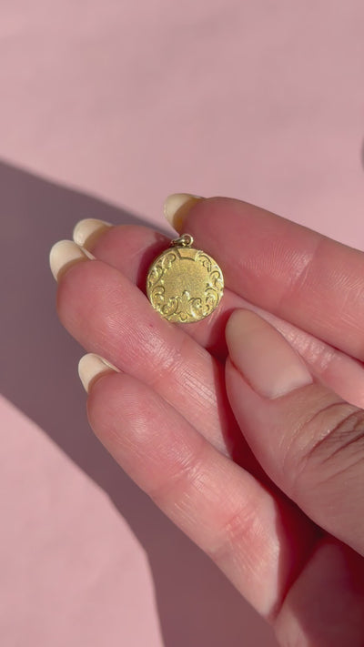 A hand holding a gold locket against a pink background