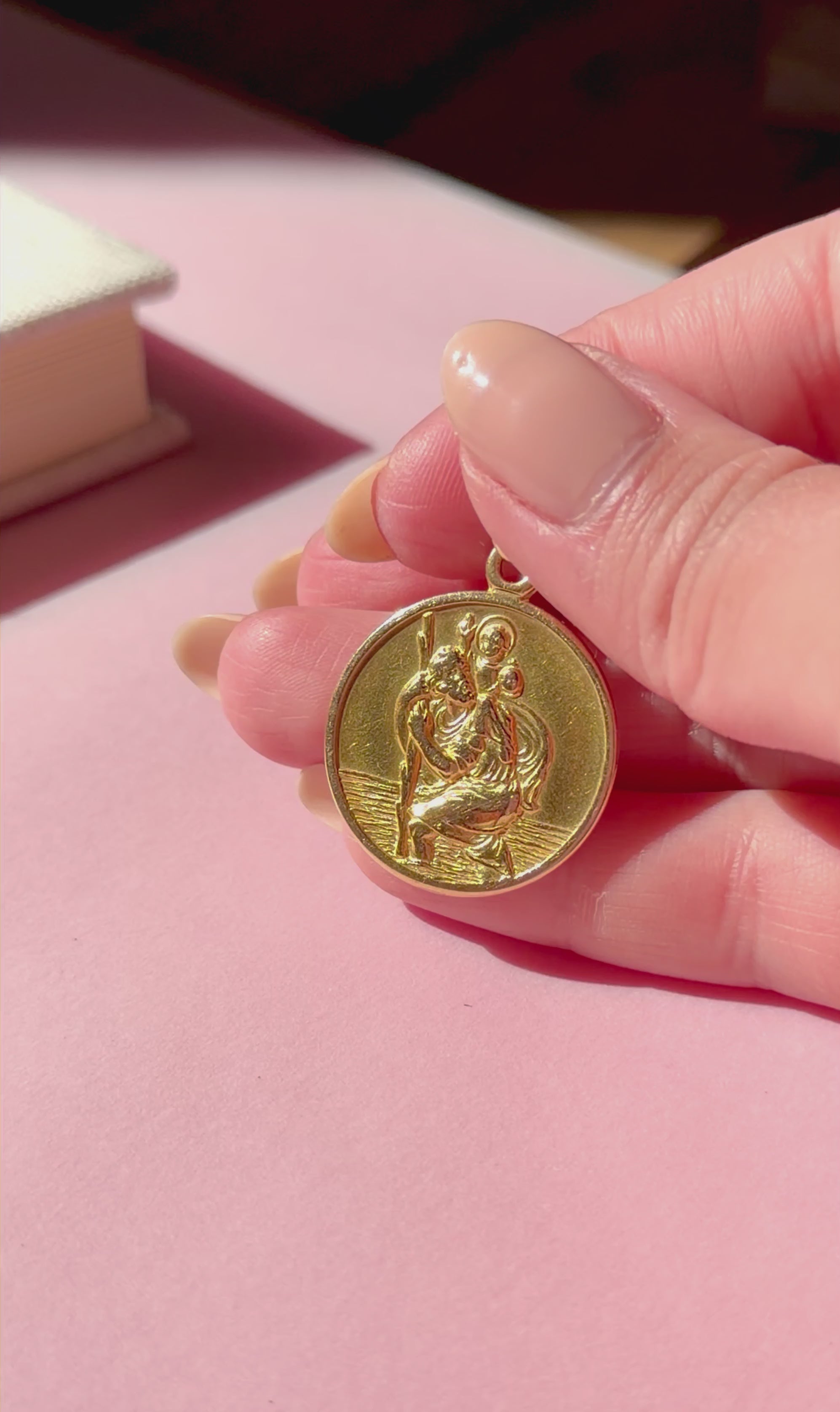 Vintage gold pendant held in a hand against a pink background