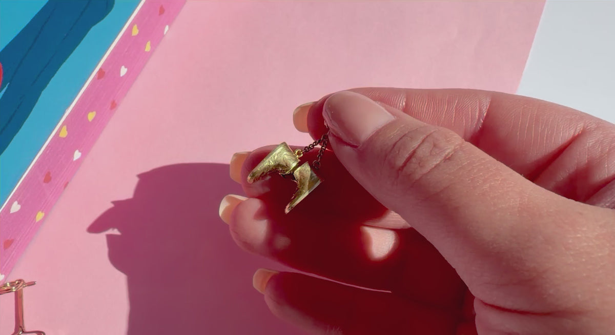 A close-up of a hand holding a gold pendant shaped like a pair of baby boots on colorful background.