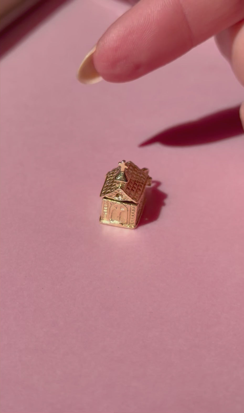 Miniature gold chapel charm on a pink background.