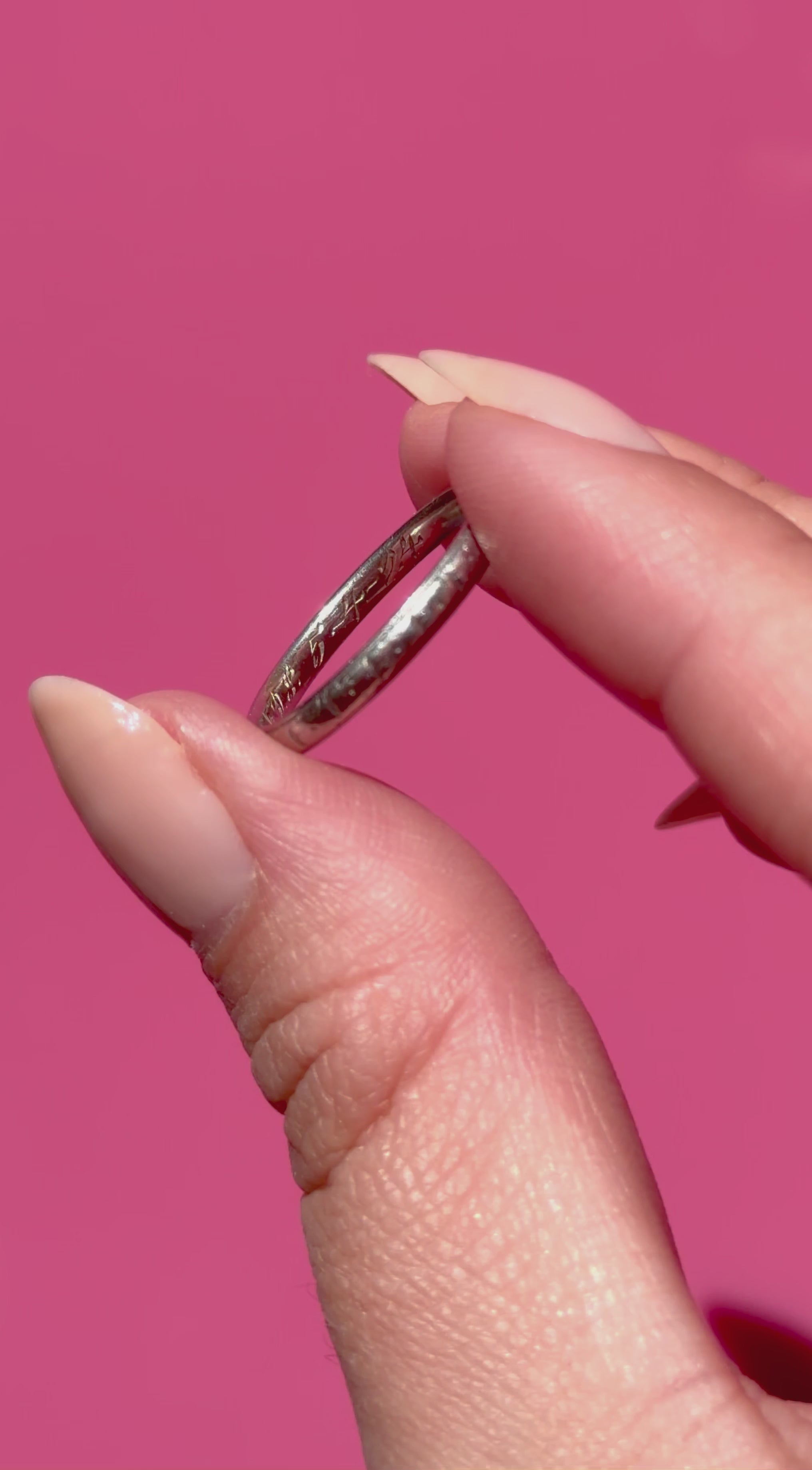 Platinum ring held between fingers against a pink background
